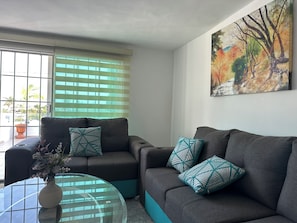 Una sala de estar con un sofá, una mesa de centro de vidrio y un cuadro en la pared.