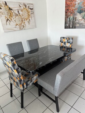 Un comedor con una mesa de mármol negro, sillas tapizadas en gris y un banco.