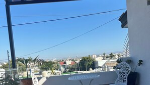 Ein Balkon mit einem weißen Metalltisch und Stühlen, einem Blumentopf und Blick auf die Stadt.