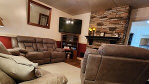 Een woonkamer met een stenen openhaard, een televisie en leren fauteuils.