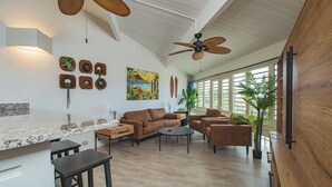 Amplia sala de estar con cocina, ventilador de techo, mesa de comedor y un ventanal grande.