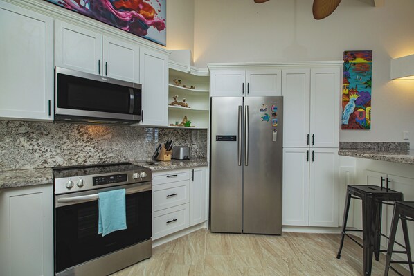 Una cocina con gabinetes blancos, un refrigerador de acero inoxidable, un microondas y una estufa.