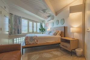A bedroom with a bed, bedside table, lamp, and a view of the outdoors.