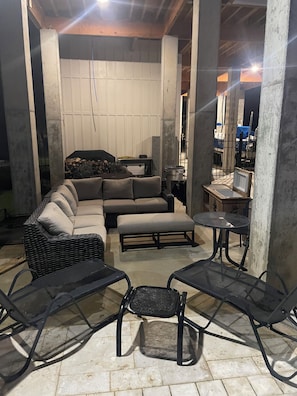 A modern outdoor seating area with a sofa, ottoman, and chairs, surrounded by columns and a tiled floor. - Luxury home HEATED pool and spa overlooking the Bay, 1 mile from the Beach. (Pass Christian)