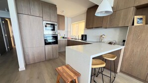 Eine moderne Küche mit Holzschränken, einem eingebauten Backofen, einer weißen Kücheninsel mit Barhocker und einer Pendelleuchte.