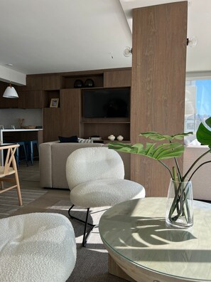 Ett modernt vardagsrum med en soffa, ett soffbord i glas och en tv som är monterad på en vägg av trä.