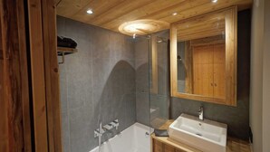 A modern bathroom with a wooden ceiling, a glass shower enclosure, a white bathtub, and a wooden vanity.