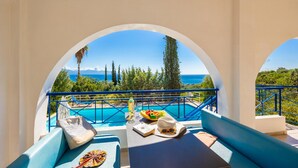 A balcony with a view of a pool and the sea, a table with a book, a hat, and a bottle. - Villa Cleo With 3 Bedrooms and 2 Bathrooms (Messini)