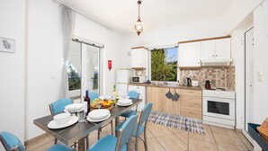 A modern kitchen with white cabinets, a dining table set for four, and a view of greenery outside. - Villa Cleo With 3 Bedrooms and 2 Bathrooms (Messini)