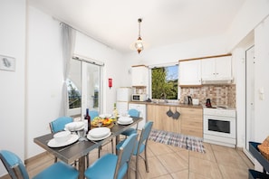 Une cuisine moderne avec des meubles blancs, une table à manger dressée pour quatre personnes et une vue sur la verdure à l’extérieur.