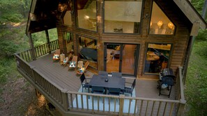 Eine zweistöckige Holzhütte mit einer Terrasse, Sitzgelegenheiten im Freien und einem sichtbaren Innenraum mit Essbereich.