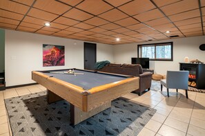 A pool table in a room with a patterned rug, a couch, a television, and a fireplace. - Secluded Chalet: Trails, EV charger, Game Room (Lancaster)