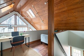 A modern loft bedroom with a sloped ceiling, skylights, a desk with a laptop, and a comfortable seating area. - Secluded Chalet: Trails, EV charger, Game Room (Lancaster)