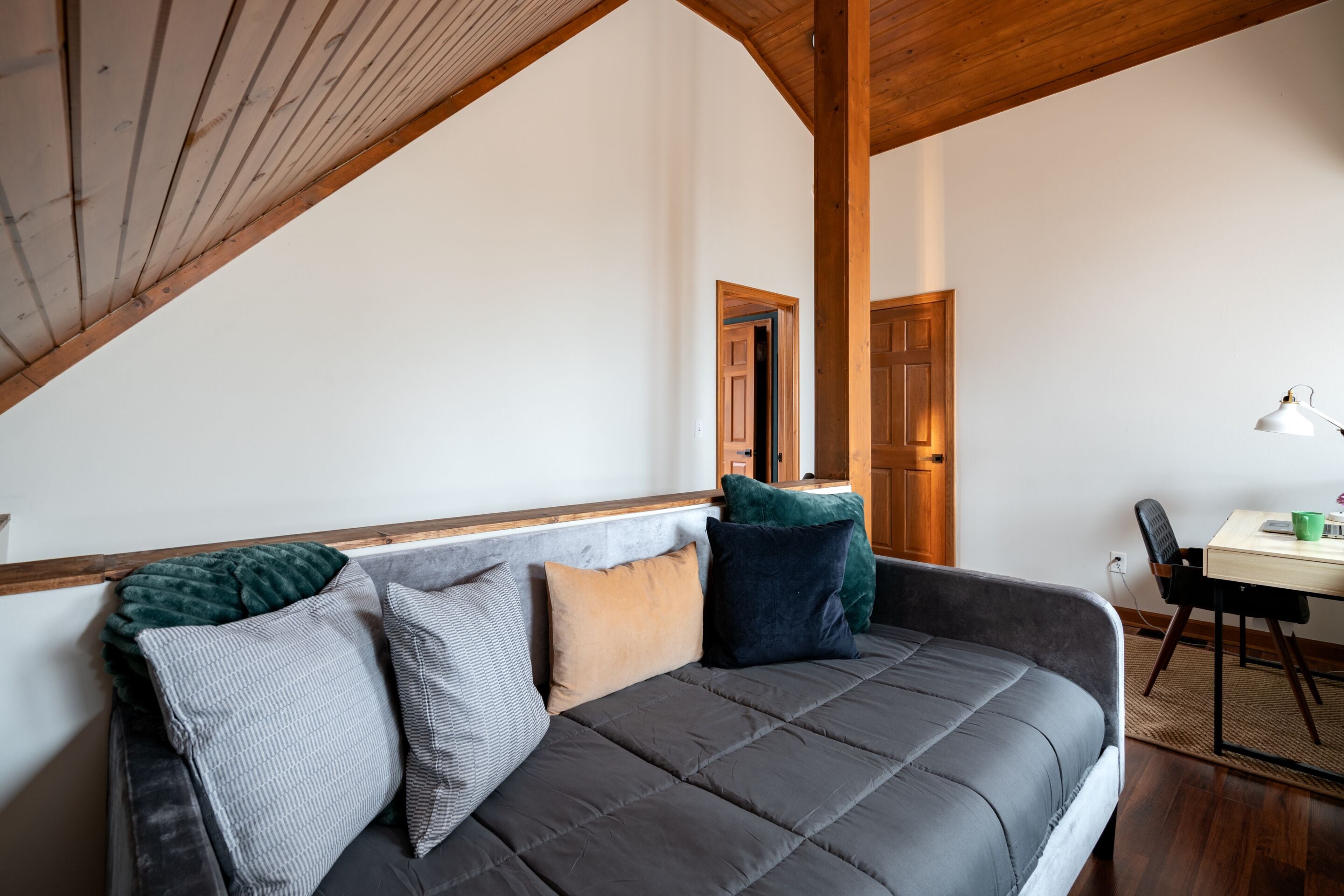A cozy room with a gray sofa, wooden beams, and a small dining area with a table and chair.