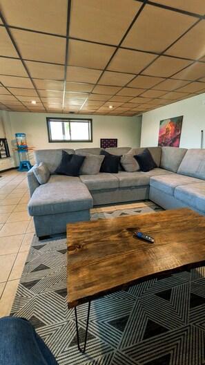 A living room with a sectional sofa, a wooden coffee table, a patterned rug, a window, and a wall-mounted artwork. - Secluded Chalet: Trails, EV charger, Game Room (Lancaster)