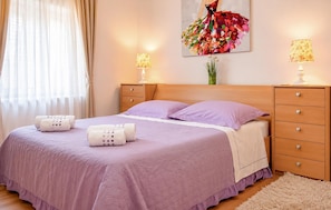 A bedroom with a bed, two bedside tables, a nightstand, a dresser, a window with curtains, and a wall-mounted painting. - Stunning home in Solin (Solin)