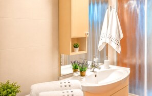 A bathroom with a sink, mirror, towel rack, and a small shelf with a plant. - Awesome home in Solin (Solin)