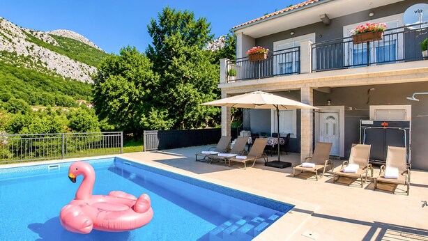 A swimming pool with a pink flamingo float, lounge chairs, and a covered seating area with umbrellas. - Awesome home in Solin (Solin)