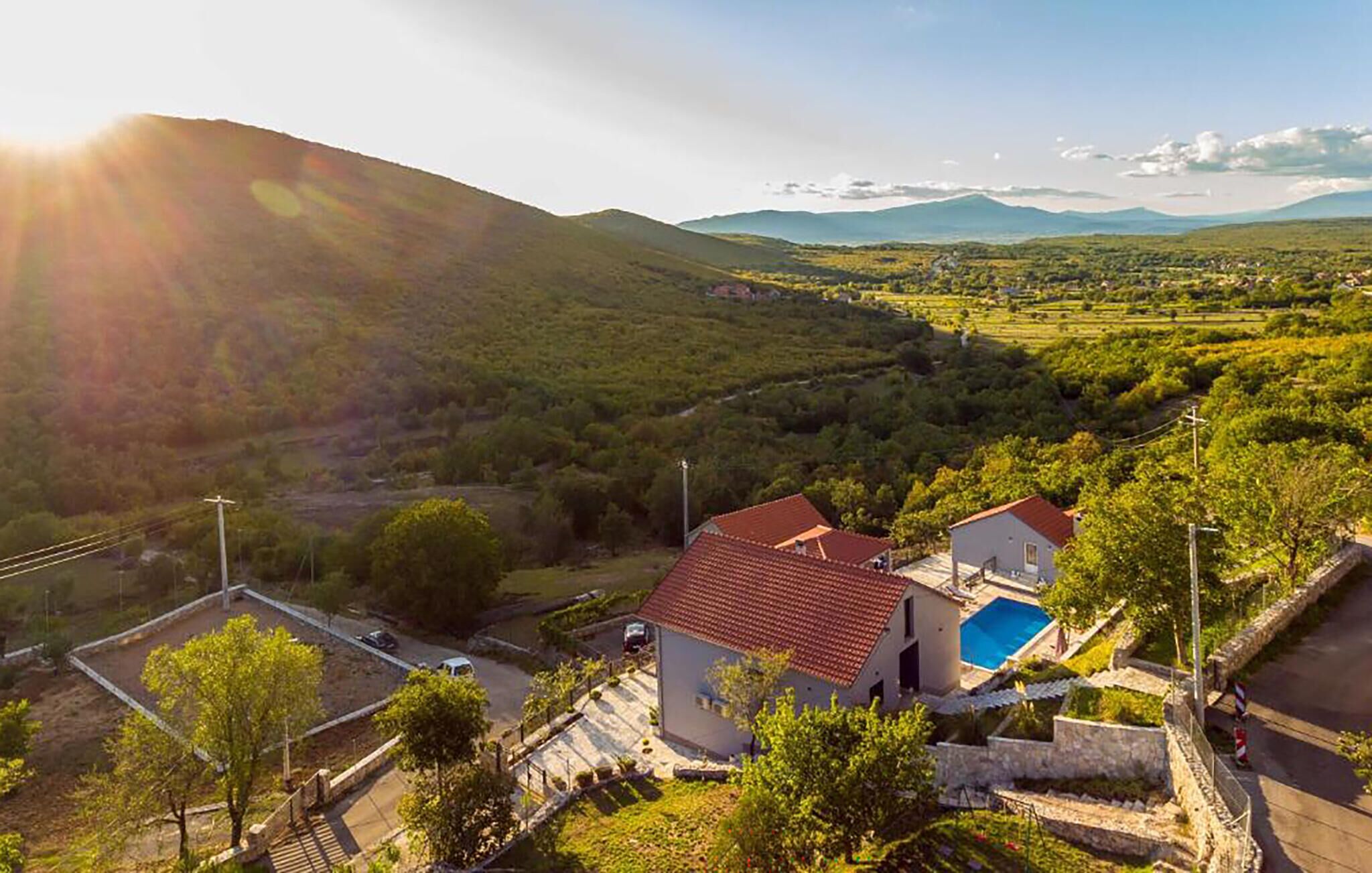 A residential area with houses, a swimming pool, and a hilly landscape in the background.