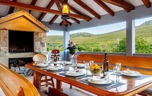 A dining table set for two with a stone fireplace, wooden beams, and a view of rolling hills. - Stunning home in Trilj (Trilj)