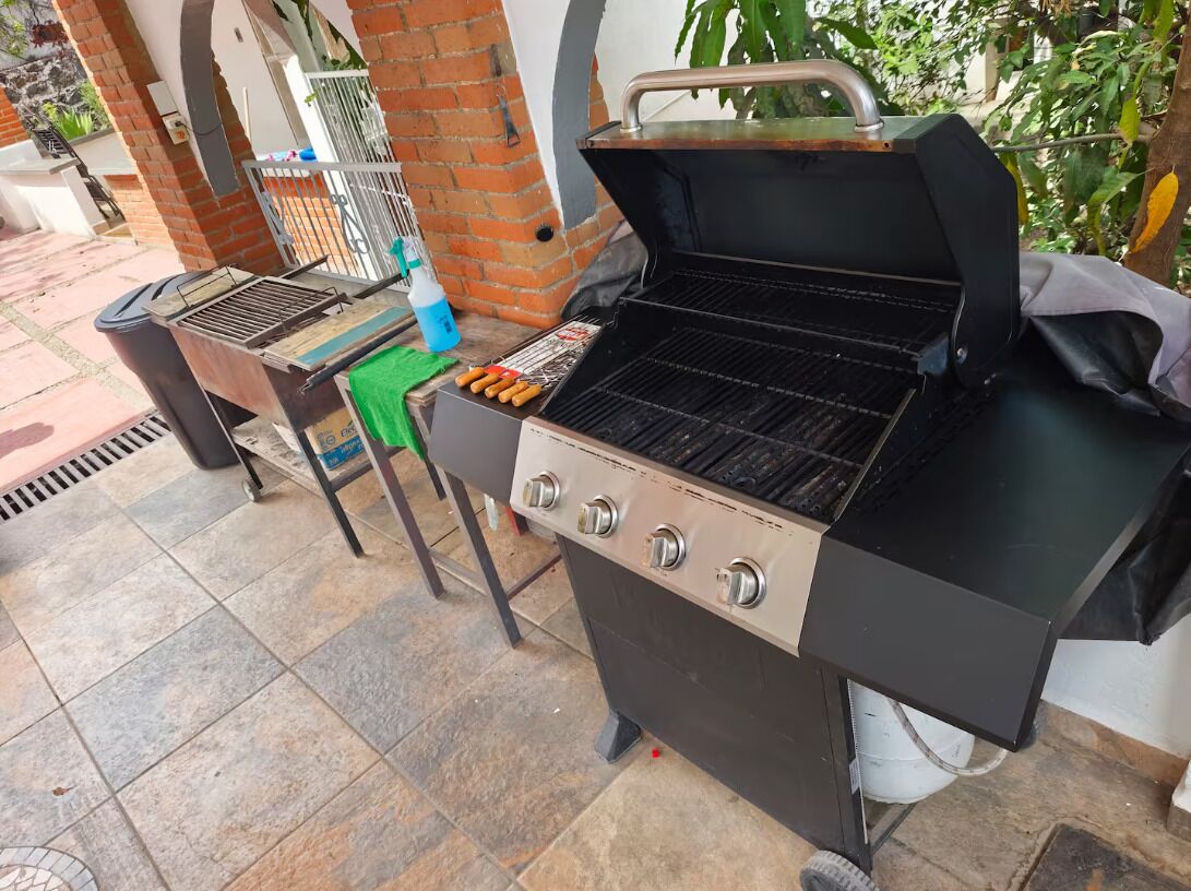 Una griglia per barbecue con quattro fuochi e un tavolino laterale con una bottiglia e utensili.