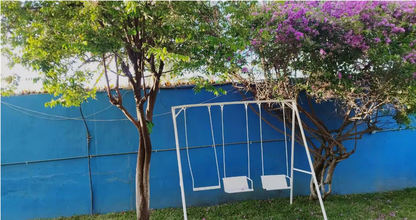 A swing set against a blue wall with trees and purple flowers.