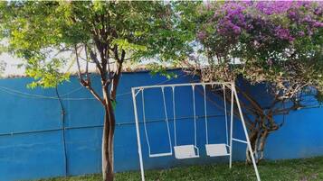 A swing set against a blue wall with trees and purple flowers.