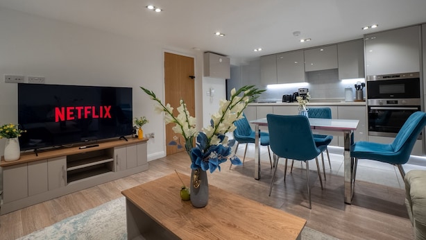 A modern living room with a flat-screen TV, a wooden coffee table, and a vase of flowers. - Cosy Battersea Flat | Zone 2 London | Sleeps 5 | Free Parking! (London)