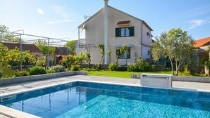 A swimming pool with a tiled deck, a house with a sloped roof, and a clear sky. - Lovely home in Lozovac (Lozovac)