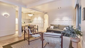 Ein modernes Wohnzimmer mit einer Couch, Sesseln, einem Essbereich und einer Küche im Hintergrund.