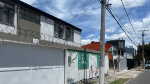 Ein Gebäude mit weißer Fassade, Stacheldraht auf dem Dach und einem Wandbild eines Fahrrads.