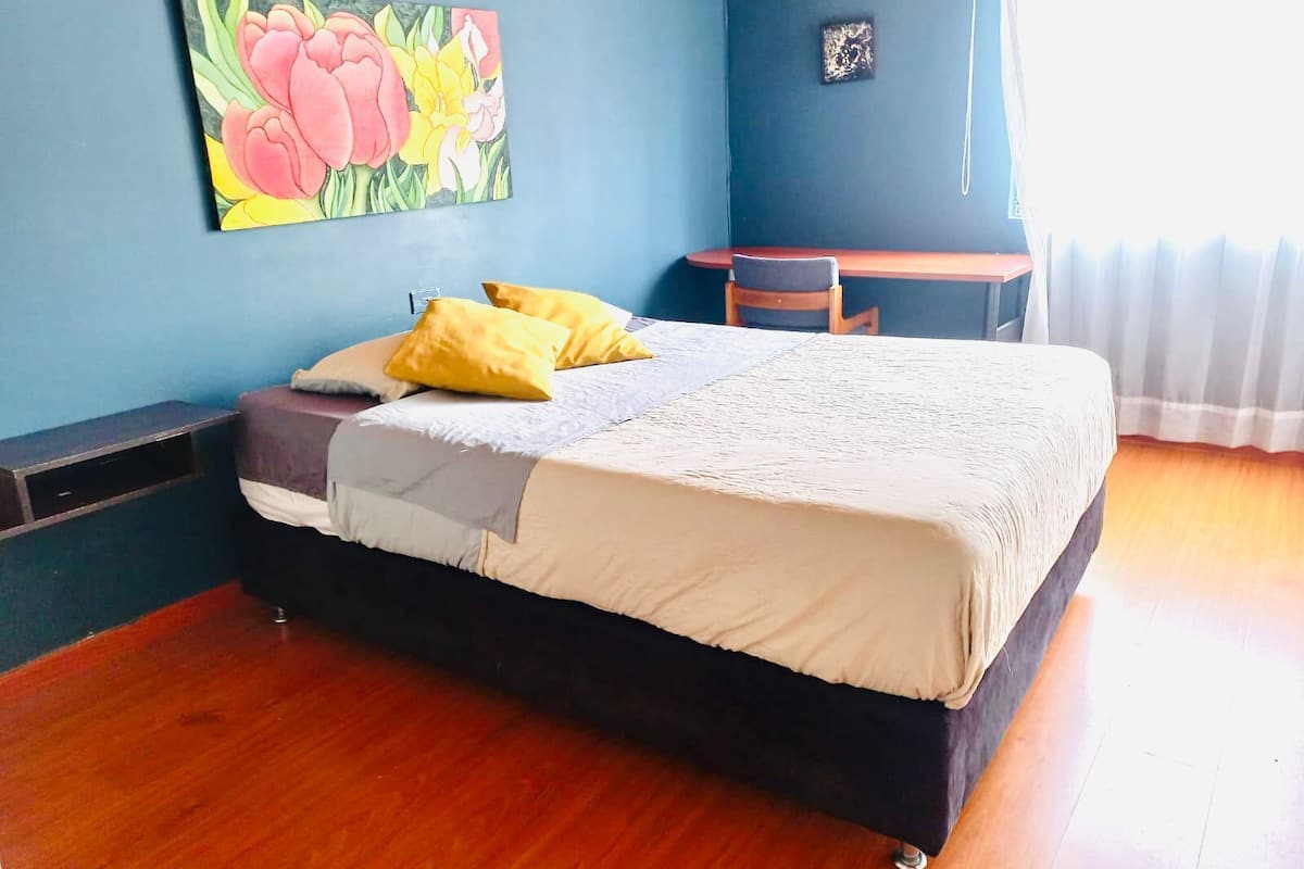 A bedroom with a bed, two yellow pillows, a desk, and a chair.