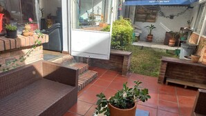 Eine Terrasse mit Korbmöbeln, Blumentöpfen und einer Glastür, die zu einem Zimmer führt.