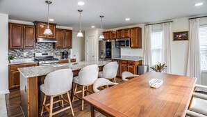 Een moderne keuken met granieten aanrechtbladen, roestvrijstalen apparatuur, houten keukenkastjes, en een eethoek met een houten tafel en stoelen.