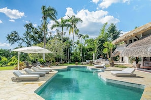 A swimming pool with lounge chairs, a thatched-roof structure, and tropical vegetation. - Ocean View Villa, Pool, Bbq, Jacuzzi, Staff Incl (La Romana)