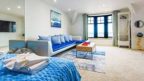Ett modernt vardagsrum med en soffa, ett soffbord, en tv och ett stort fönster med gardiner.