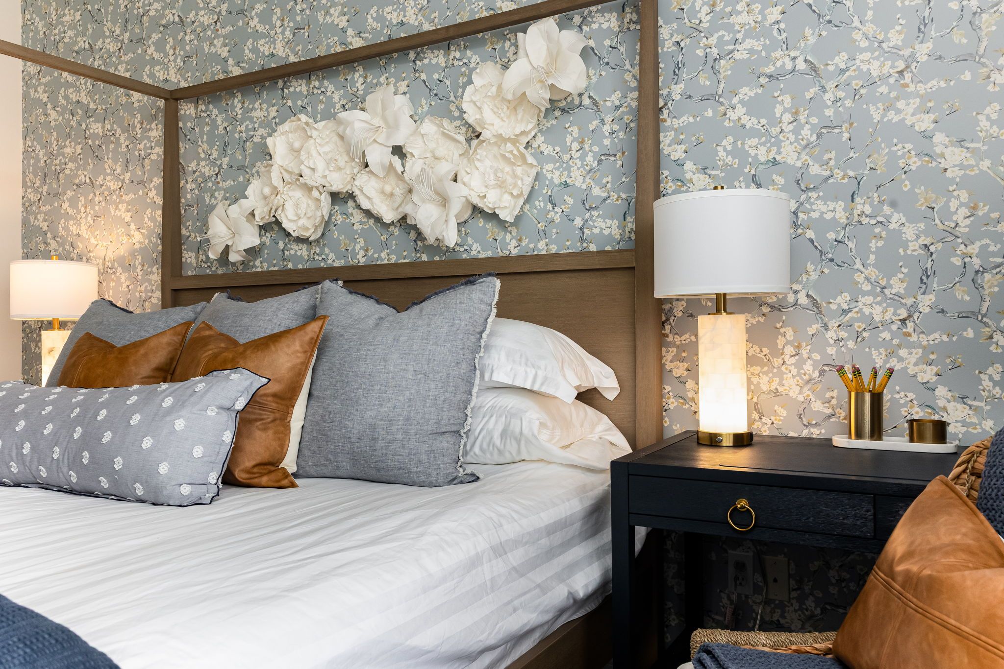 Un lit bien fait, avec une tête de lit, une table de chevet avec une lampe et un papier peint à motifs floraux.