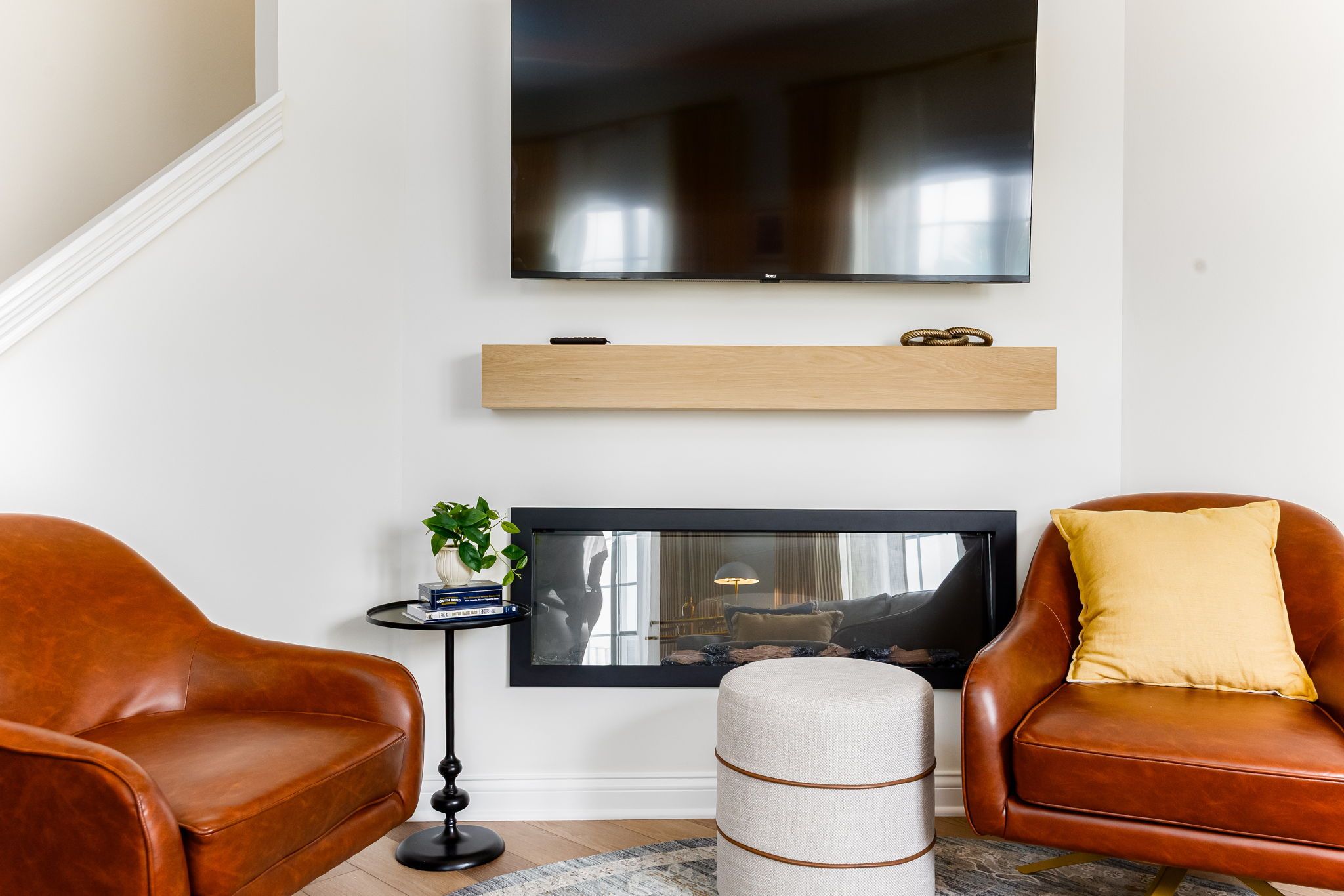 Un salon doté d’un téléviseur à écran plat, de fauteuils en cuir, d’une petite table d’appoint avec une plante et d’une cheminée.