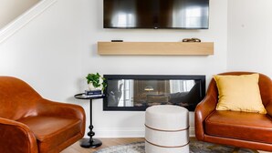 Ein Wohnzimmer mit Flachbildfernseher, Ledersessel, einem kleinen Beistelltisch mit Pflanze und Kamin.
