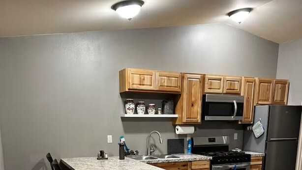 A kitchen with wooden cabinets, a granite countertop, a stainless steel refrigerator, and a microwave. - Adventure Stay Unit 2 (Palmer)