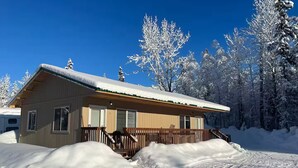 A wooden cabin with a porch, surrounded by snow-covered trees. - Adventure Stay Unit 2 (Palmer)