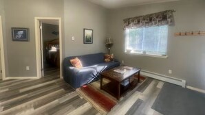 A living room with a sofa, coffee table, and a window with blinds. - Adventure Stay Unit 2 (Palmer)