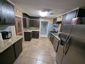 A kitchen with granite countertops, dark cabinetry, a stainless steel refrigerator, and a tiled floor.