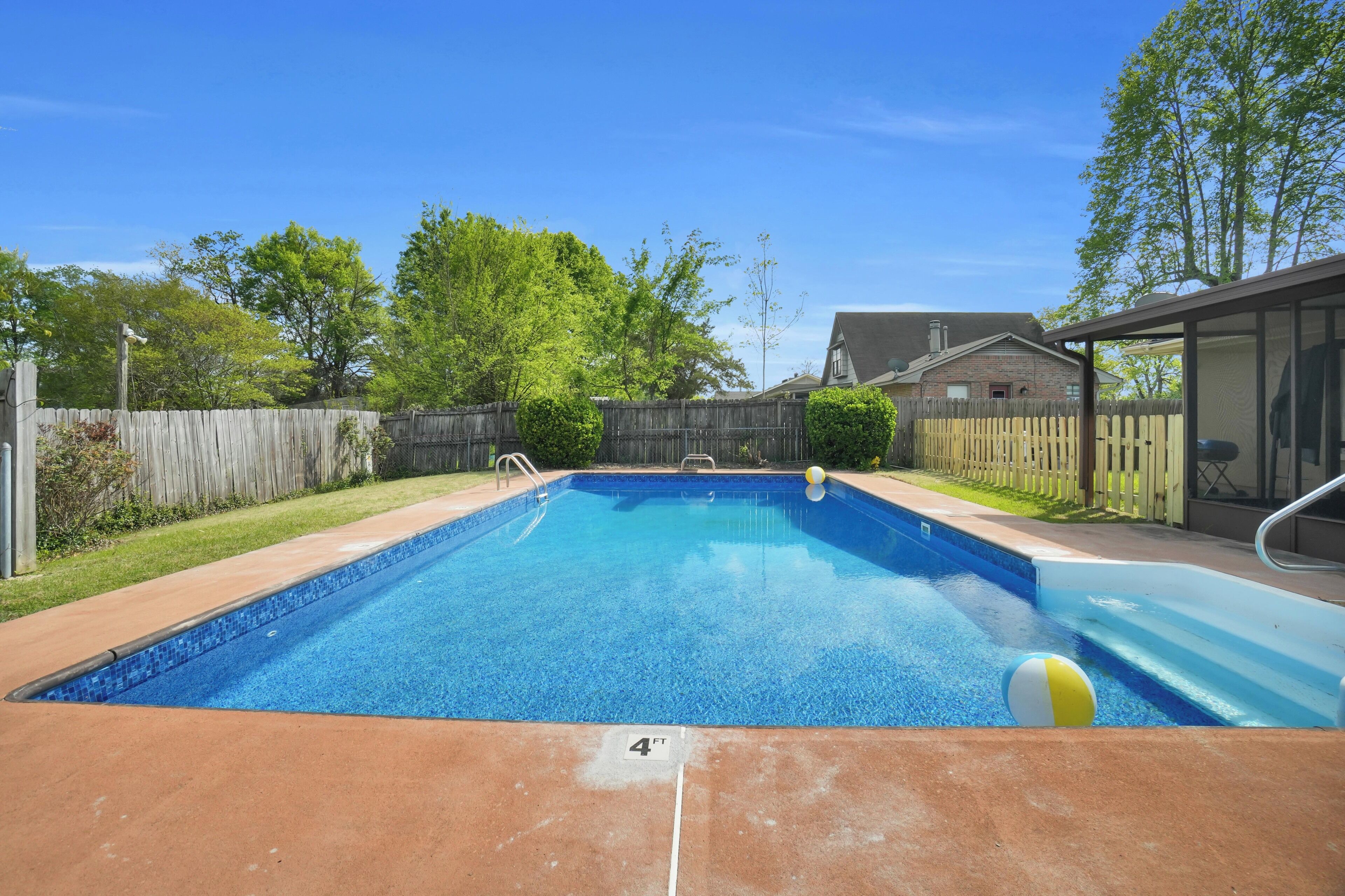 Piscina rectangular con revestimiento azul, rodeada por una valla de madera y una zona cubierta a la derecha.