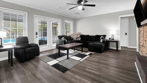 Una sala moderna con un sofá de cuero negro, un sillón reclinable, una mesa de centro y un ventilador de techo.