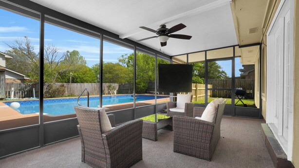 Un patio cubierto con ventilador de techo, mobiliario de mimbre, televisor de pantalla plana y vista a una piscina.