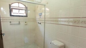 A bathroom with a toilet, a shower, and a window. - Hotel e Pousada Naturalis (Paranaguá)