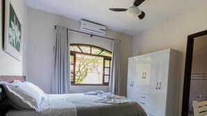 A bedroom with a bed, an air conditioning unit, a wardrobe, and a window with curtains. - Hotel e Pousada Naturalis (Paranaguá)