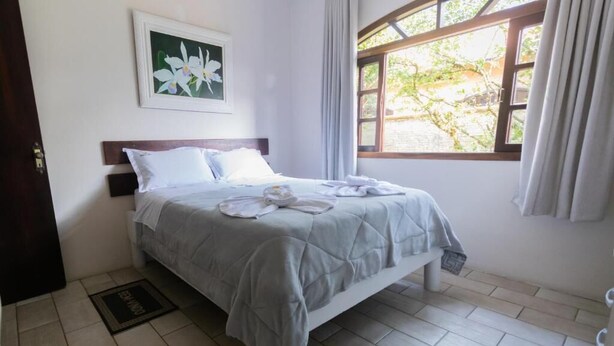 A neatly made bed with a grey quilt, white pillows, and a framed floral artwork above it. - Hotel e Pousada Naturalis (Paranaguá)