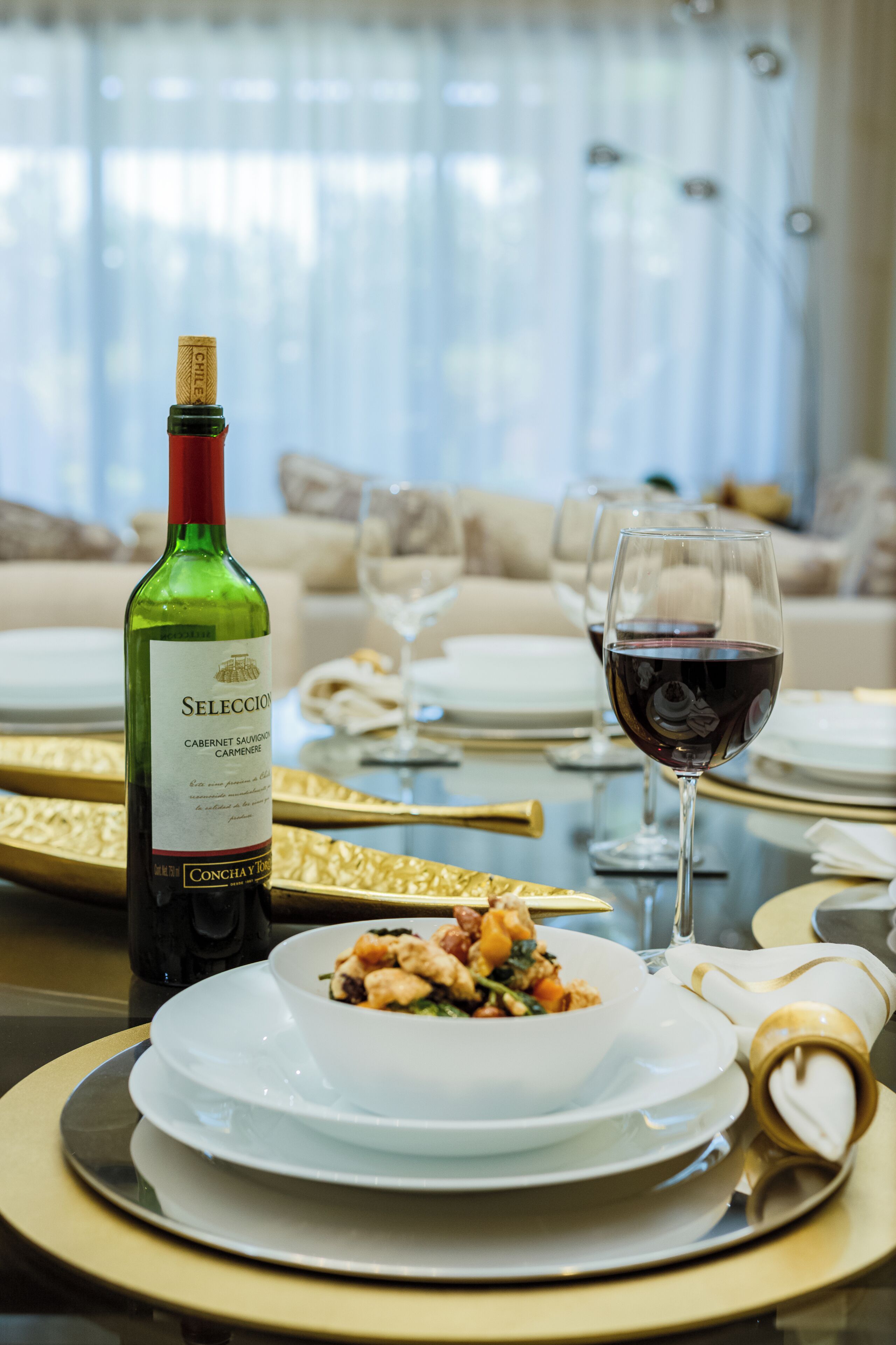 Un tavolo da pranzo con una bottiglia di vino, un bicchiere di vino rosso e una ciotola di cibo.